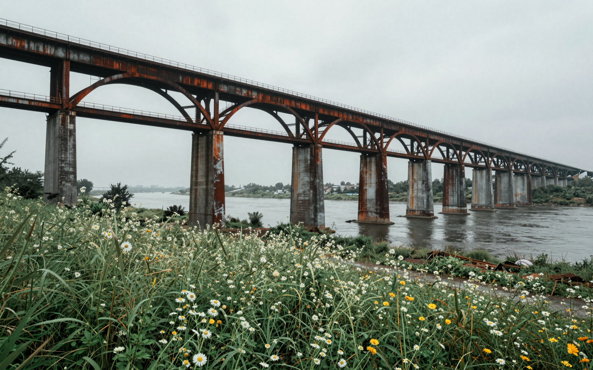 Rustic Steel Arch Bridge Over River with Wildflowers in Foreground