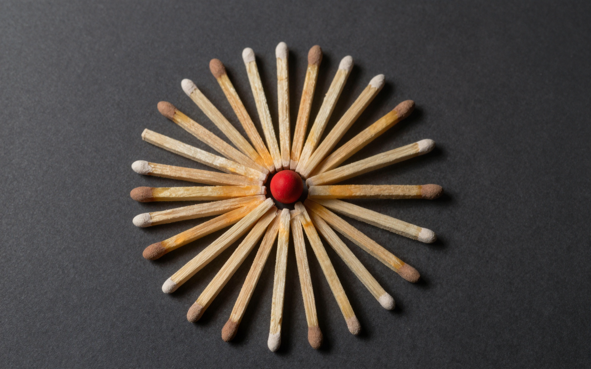Circular Matchstick Arrangement with Red Center on Dark Surface
