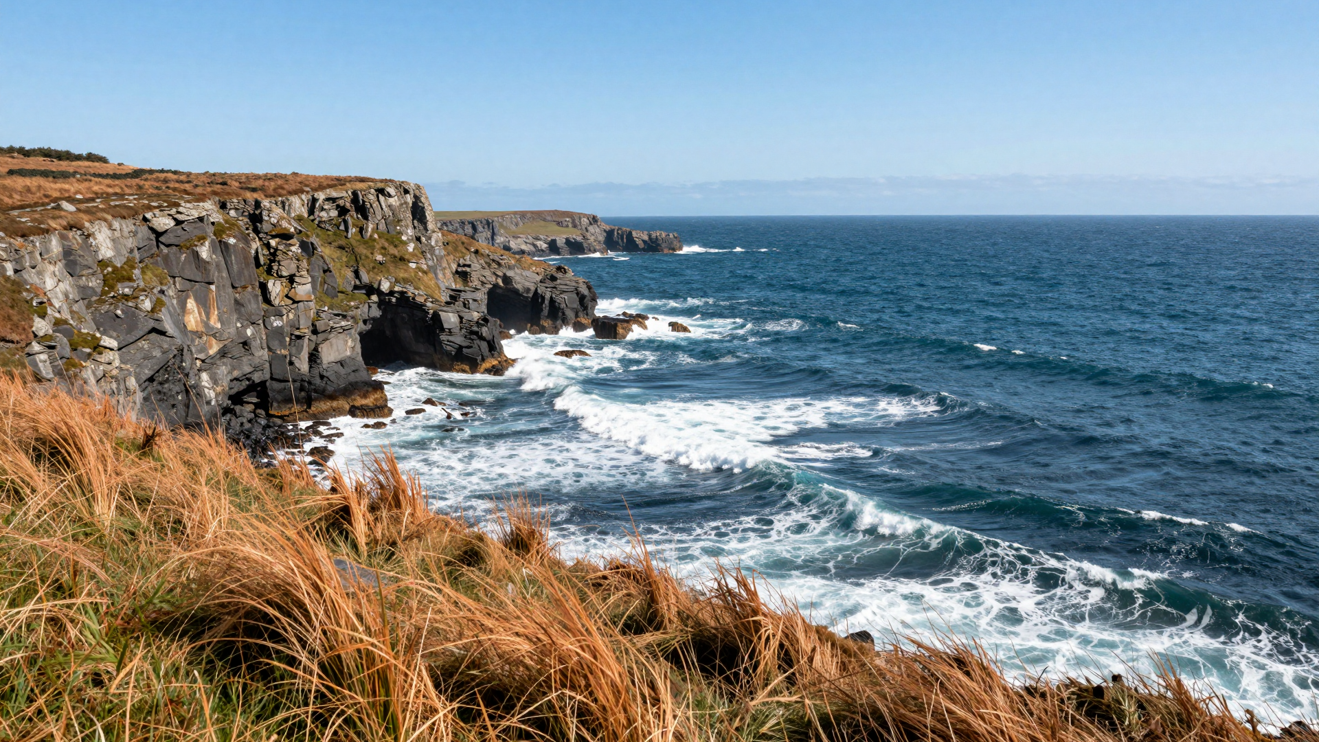 Rocky Coastal Cliffs and Waves Beneath a Clear Blue Sky